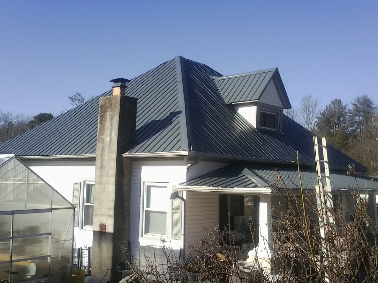 Dark blue standing seam metal roof on a white farmhouse with dormer — Slate & Tile Roof Repair by Roofing Brothers in North Apollo
