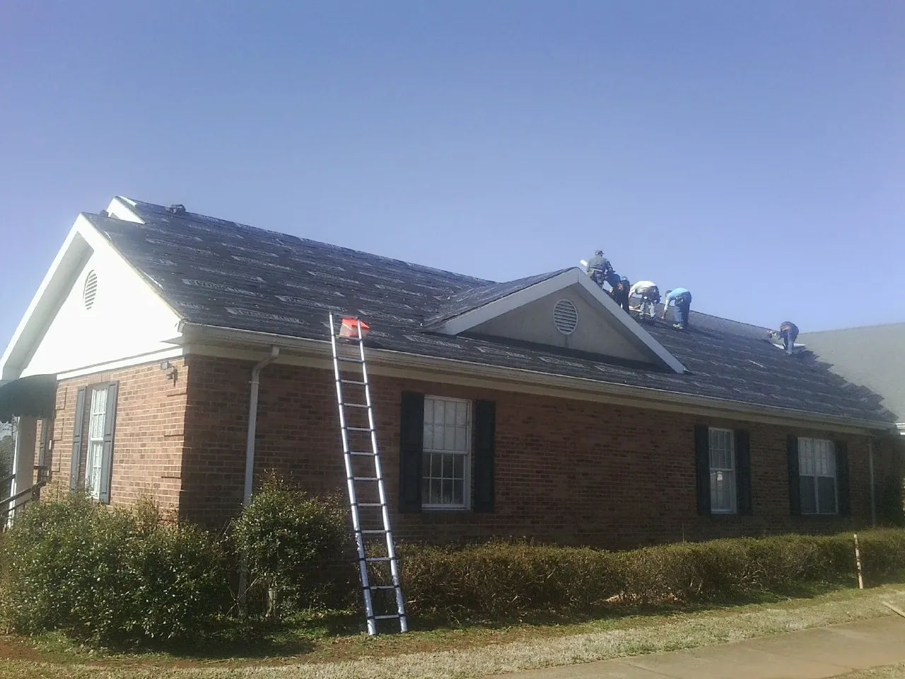 Crew tearing shingles off a brick ranch roof with a ladder set — Metal Roof Repair work by our crew in North Apollo