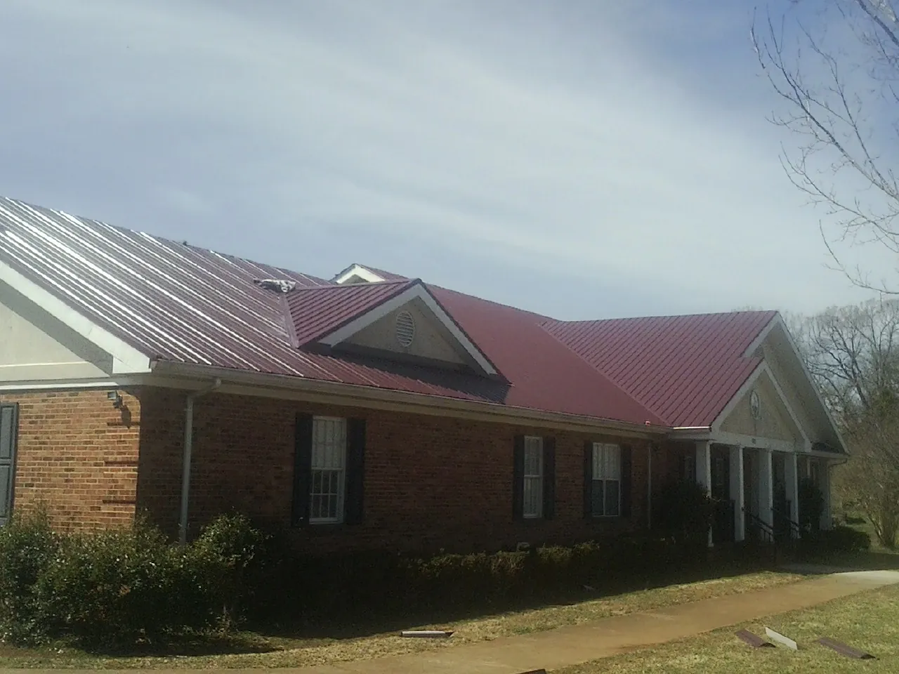 Red metal roof with gabled entries on a long brick building, from a Hail Damage Roof Repair job in North Apollo