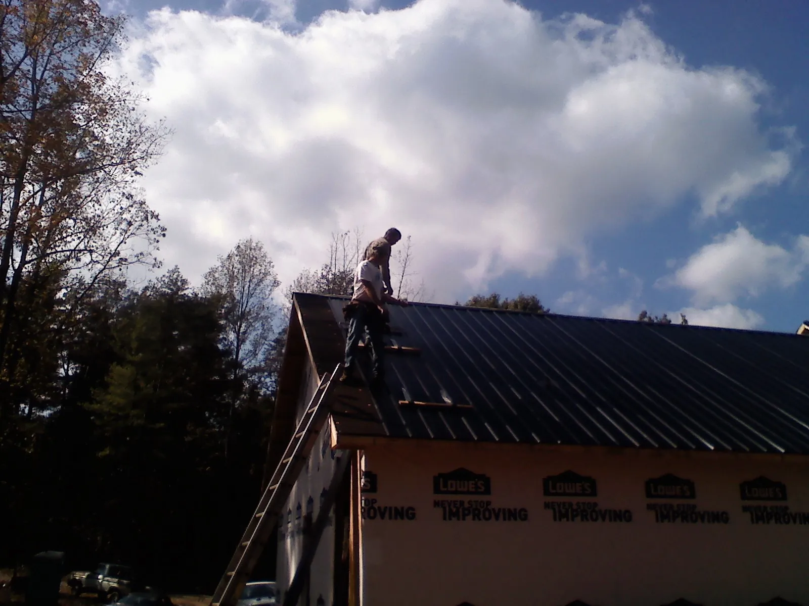 Roofer fastening dark metal panels high against a cloudy sky, from a Roof Inspection job in North Apollo
