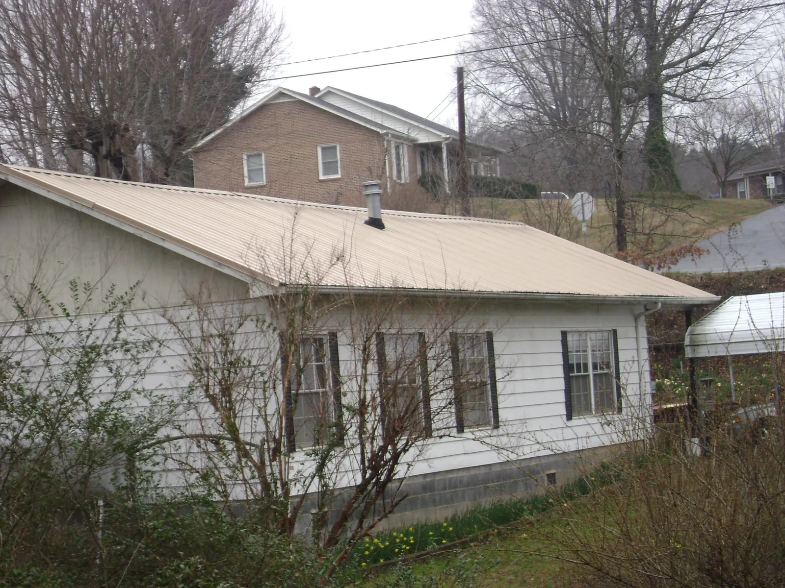 Tan metal roof on a white sided house set into a hillside — Commercial Roofing by Roofing Brothers in North Apollo
