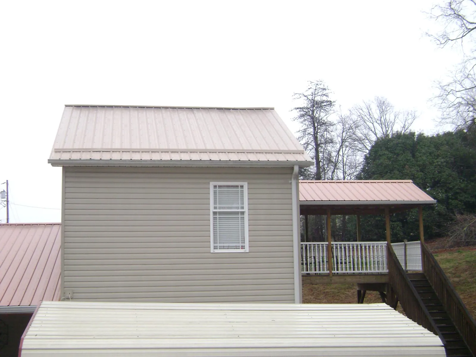 Tan metal roofs on a two story addition and attached porch, from a Roof Replacement job in North Apollo